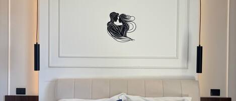 A bedroom with a bed, two nightstands, a wall-mounted artwork, and a ceiling light fixture.