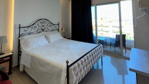 A modern hotel room with a large bed, a desk, and a balcony with outdoor seating. - IG - Villa Don Antonio  Apartment  (Giardini Naxos)