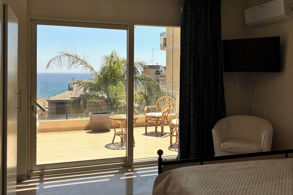 Ein Hotelzimmer mit Balkon, einem Bett, einem Fernseher und Meerblick.