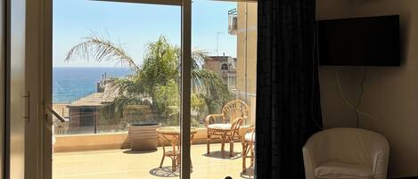 A hotel room with a balcony, a bed, a TV, and a view of the sea.