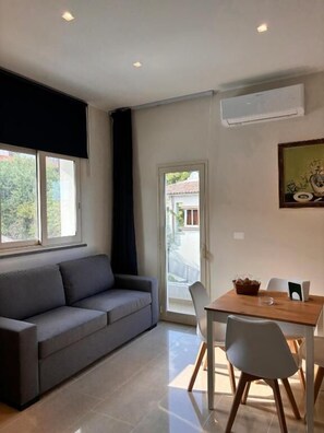 Una sala de estar moderna con un sofá, una mesa de comedor, sillas y una ventana.