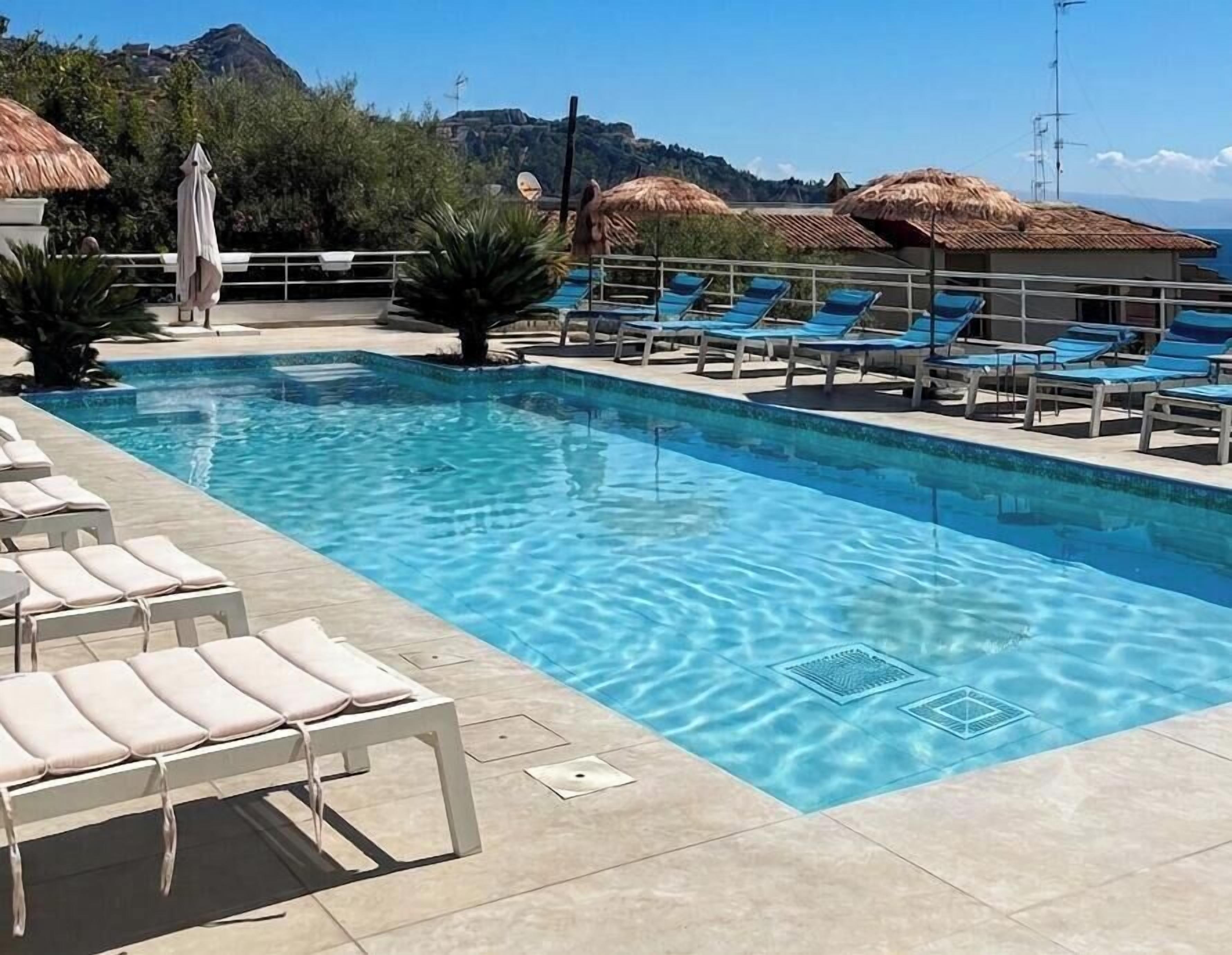 Ein Pool mit Liegestühlen und Sonnenschirmen, umgeben von einer gefliesten Terrasse.