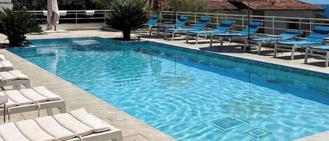 Une piscine entourée d’une terrasse carrelée, avec des chaises longues et des parasols.