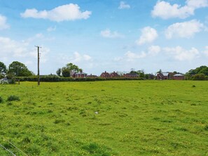 A rural landscape with a green field, a power line, and a row of houses in the background. - 2 bedroom accommodation in Burgh Le Marsh (Burgh Le Marsh)
