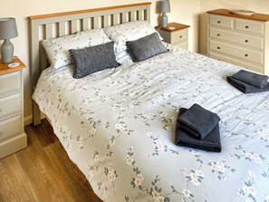 A neatly made bed with floral bedding, a wooden headboard, a bedside table with a lamp, and a nightstand with a lamp. - 2 bedroom accommodation in Burgh Le Marsh (Burgh Le Marsh)