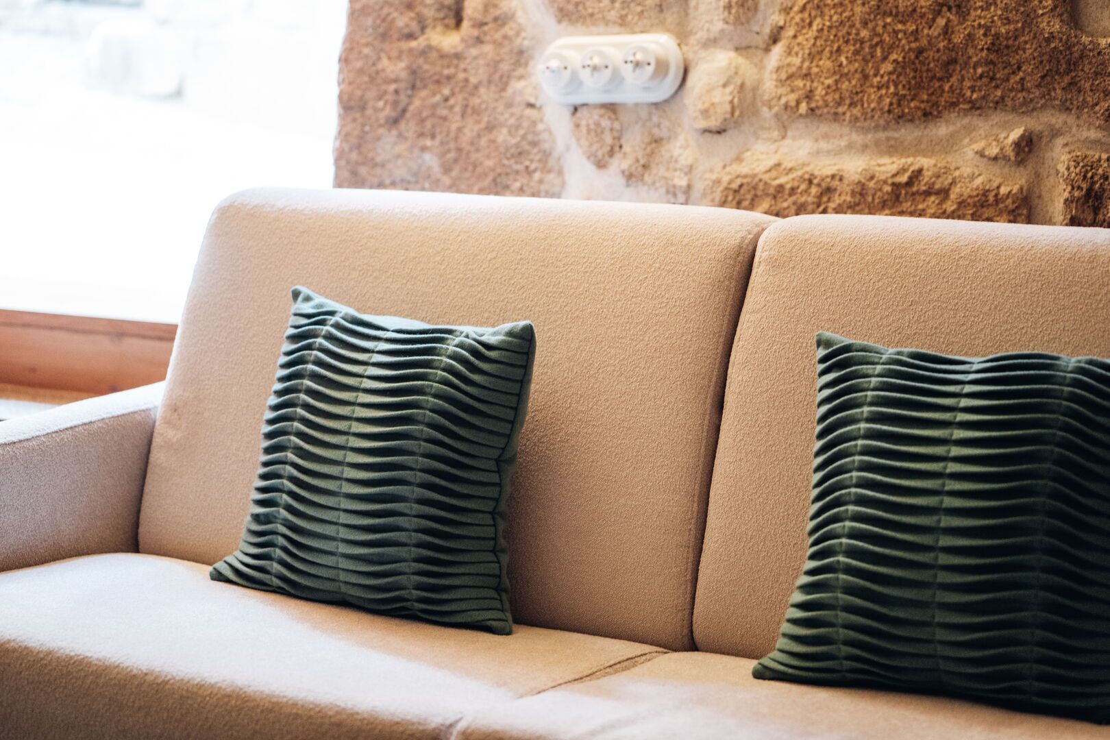 En beige sofa med to grønne puder foran en væg med struktur.