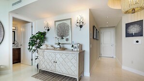 A hallway with a white cabinet, a large plant, and wall-mounted artwork. - Charming 3-bedroom condo  (West Palm Beach)