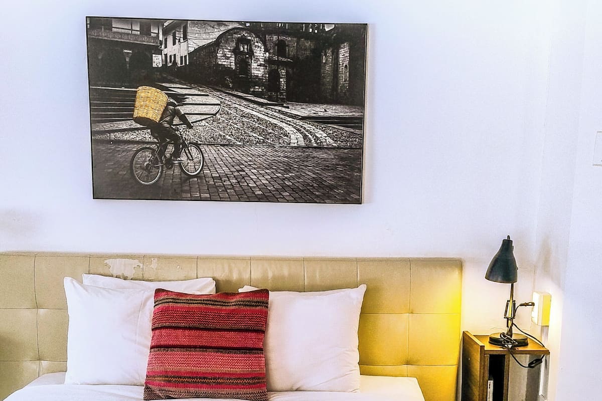 A hotel room with a bed, a headboard, a nightstand, a lamp, and a wall-mounted picture.