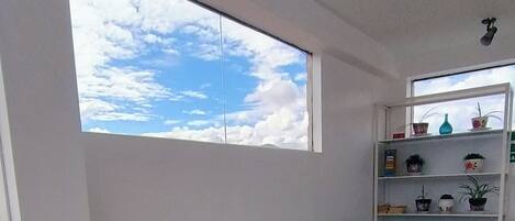 Una sala de estar con un sofá, una mesa con un florero, una estantería y un ventanal con vistas al cielo.