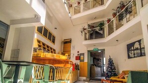 A spacious atrium with a high ceiling, multiple levels, and a central staircase. There are seating areas with chairs and tables, and a Christmas tree is visible. - Central Market Hotel San Pedro (Cusco)