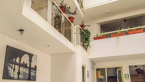 A spacious living area with a yellow sofa, a green armchair, and a coffee table. There are multiple potted plants on balconies and a large window providing natural light. - Central Market Hotel San Pedro (Cusco)