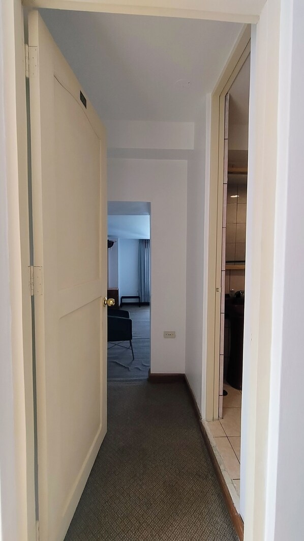 A narrow hallway with carpeted flooring leading to a room with a bed and a window. - Central Market Hotel San Pedro (Cusco)