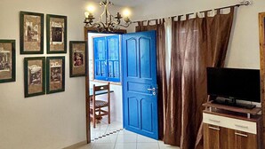 A bedroom with a bed, a television on a wooden stand, a chandelier, and a blue door. - Room Sidi bou Said (Hergla)