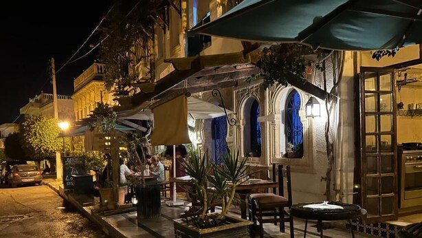 An outdoor seating area with tables and chairs, potted plants, and a building with arched windows and a door. - Room Sidi bou Said (Hergla)