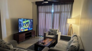 A living room with a flat-screen TV, a sofa, a coffee table, and a lamp.
