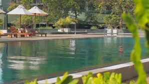 A swimming pool with a person in the water, surrounded by lounge chairs and umbrellas.