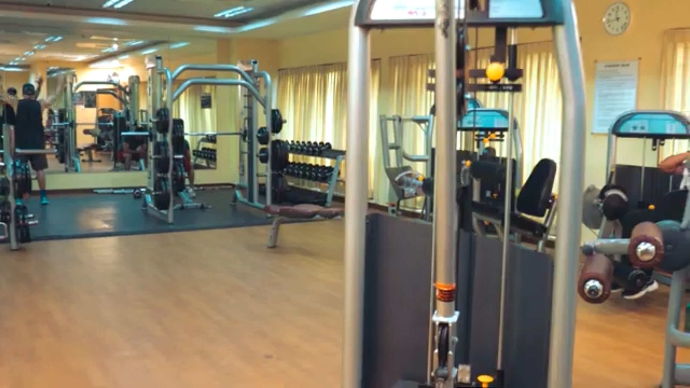 A gym with various exercise equipment, a large mirror, and a clock on the wall.