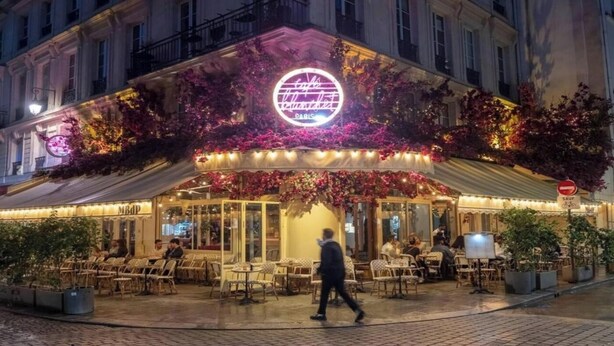 Un caffè con tavolini all'aperto, un neon e un cartello con scritto 'Saut'.