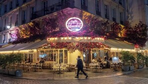 Um café com mesas ao ar livre, um letreiro de neon e um aviso com a palavra 'Saut'.