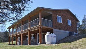 A two-story house with a balcony, a stone foundation, and two propane tanks labeled "STINSO" in front.