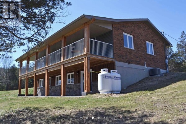 Une maison à deux étages avec un balcon, des fondations en pierre et deux réservoirs de propane portant l’inscription « STINSO » à l’avant.