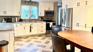 A modern kitchen with white cabinets, a stainless steel refrigerator, a microwave, and a dining area with a wooden table and chairs.