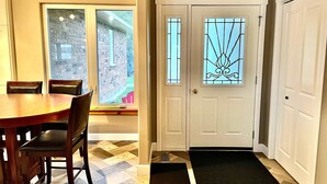 A dining area with a wooden table and chairs, a window with a view of a brick wall, and a door with a decorative glass panel.
