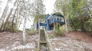 A wooden staircase leading to a blue house surrounded by trees. - Cozy cottage nestled along 90ft of pristine Georgian Bay pebble beachfront (Wiarton)
