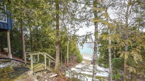 A wooden staircase leading to a dock, surrounded by trees and a body of water. - Cozy cottage nestled along 90ft of pristine Georgian Bay pebble beachfront (Wiarton)