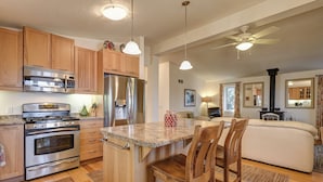 A modern kitchen with wooden cabinets, stainless steel appliances, and a central island with bar stools. - Cozy cottage nestled along 90ft of pristine Georgian Bay pebble beachfront (Wiarton)
