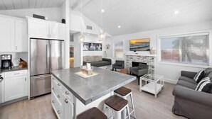 A modern kitchen with white cabinetry, a stainless steel refrigerator, and a central island with stools. - Good Day Sunshine Cottage-Newly updated!! Light and Airy w parking  (Newport Beach)