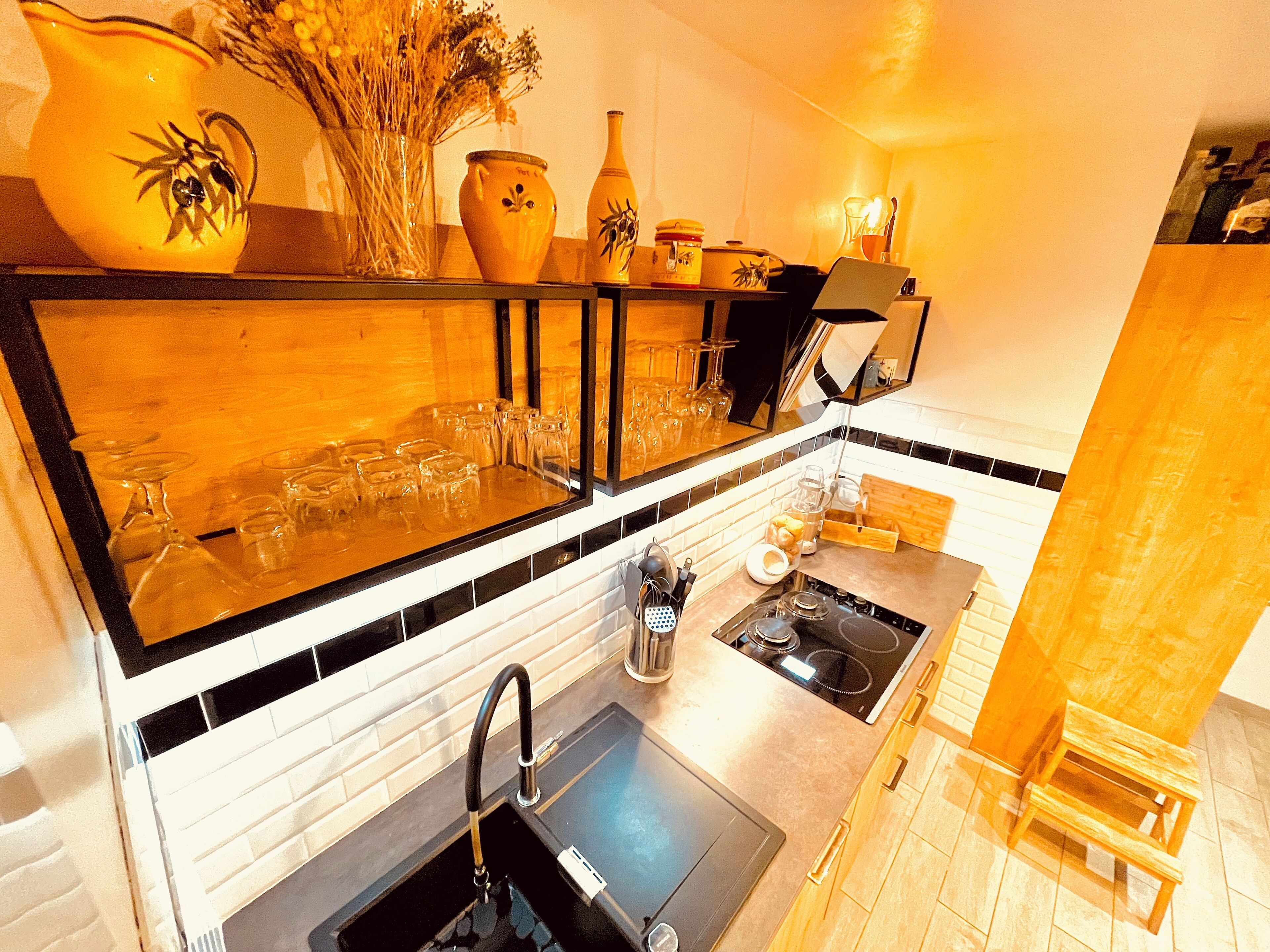 A kitchen with a black countertop, a sink, and a stove. There are various kitchen items on the counter, including a vase, a bottle, and a coffee maker.