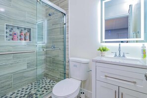 A modern bathroom with a glass-enclosed shower, a toilet, a sink with a mirror above it, and toiletries on the countertop. - 2b2b APT Close to Rose Parade and Pasadena Oldtown (Altadena)