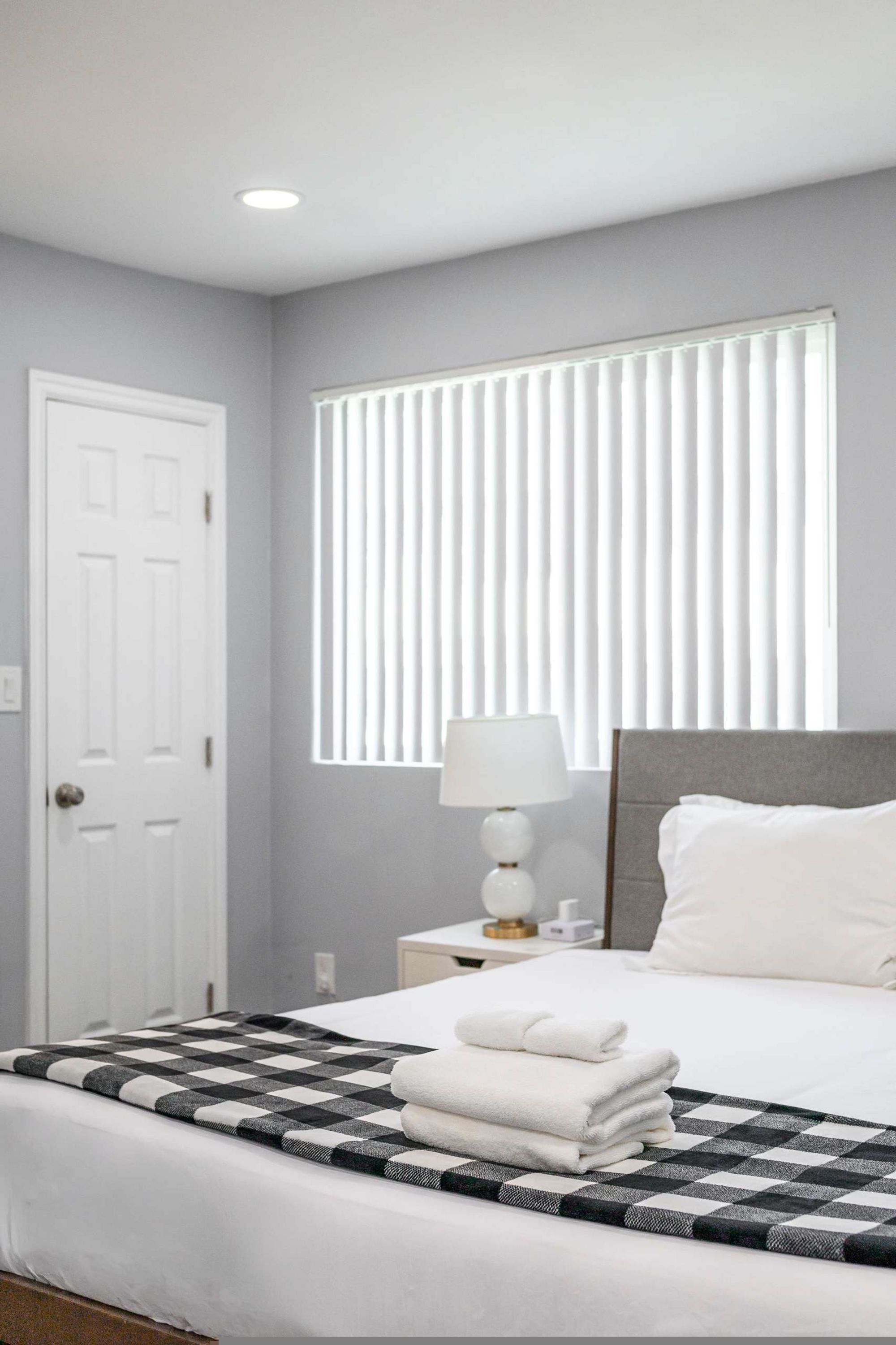 A hotel room with a bed, a nightstand with a lamp, and a window with blinds.