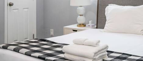 A hotel room with a bed, a nightstand with a lamp, and a window with blinds.