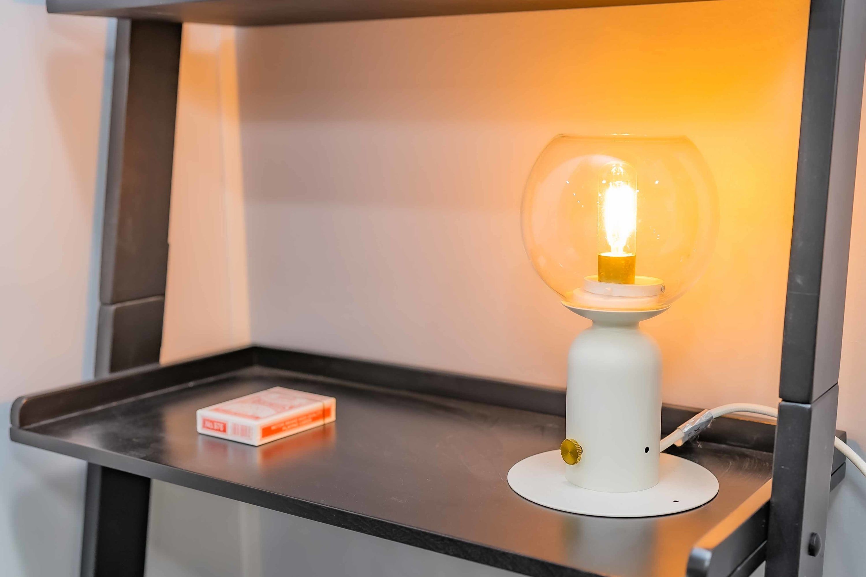 A white table lamp with a glass shade on a metallic surface.