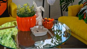 Une table en verre ornée d’une plante en pot, d’une figurine de lapin en céramique et d’une décoration en forme de citrouille.