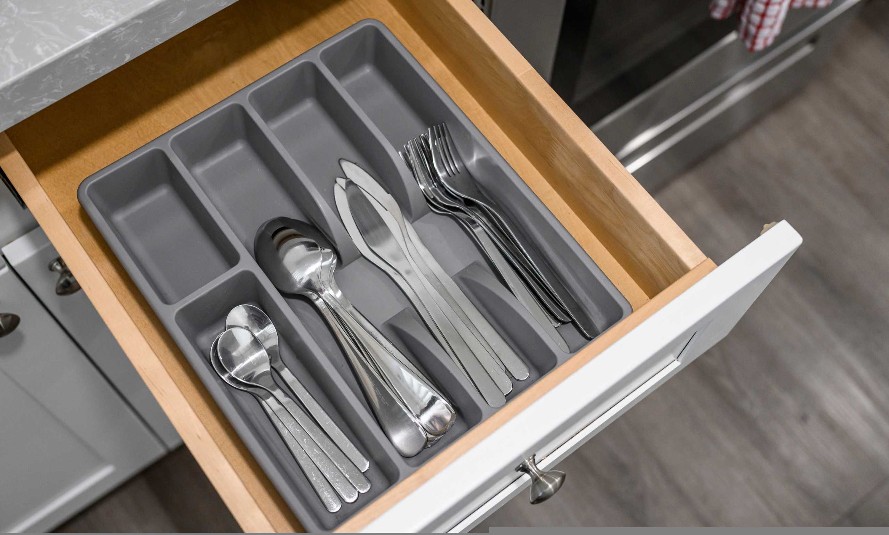 A kitchen drawer with utensils including spoons, a knife, and forks.