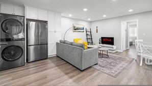 Une cuisine moderne dotée d’appareils électroménagers en acier inoxydable, d’un canapé gris, d’un coin repas blanc et d’un téléviseur à écran plat affichant le logo « NETFLIX ».