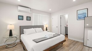 Una habitación de hotel moderna con una cama grande, lámparas de noche, una mesa de vidrio y vista al pasillo.