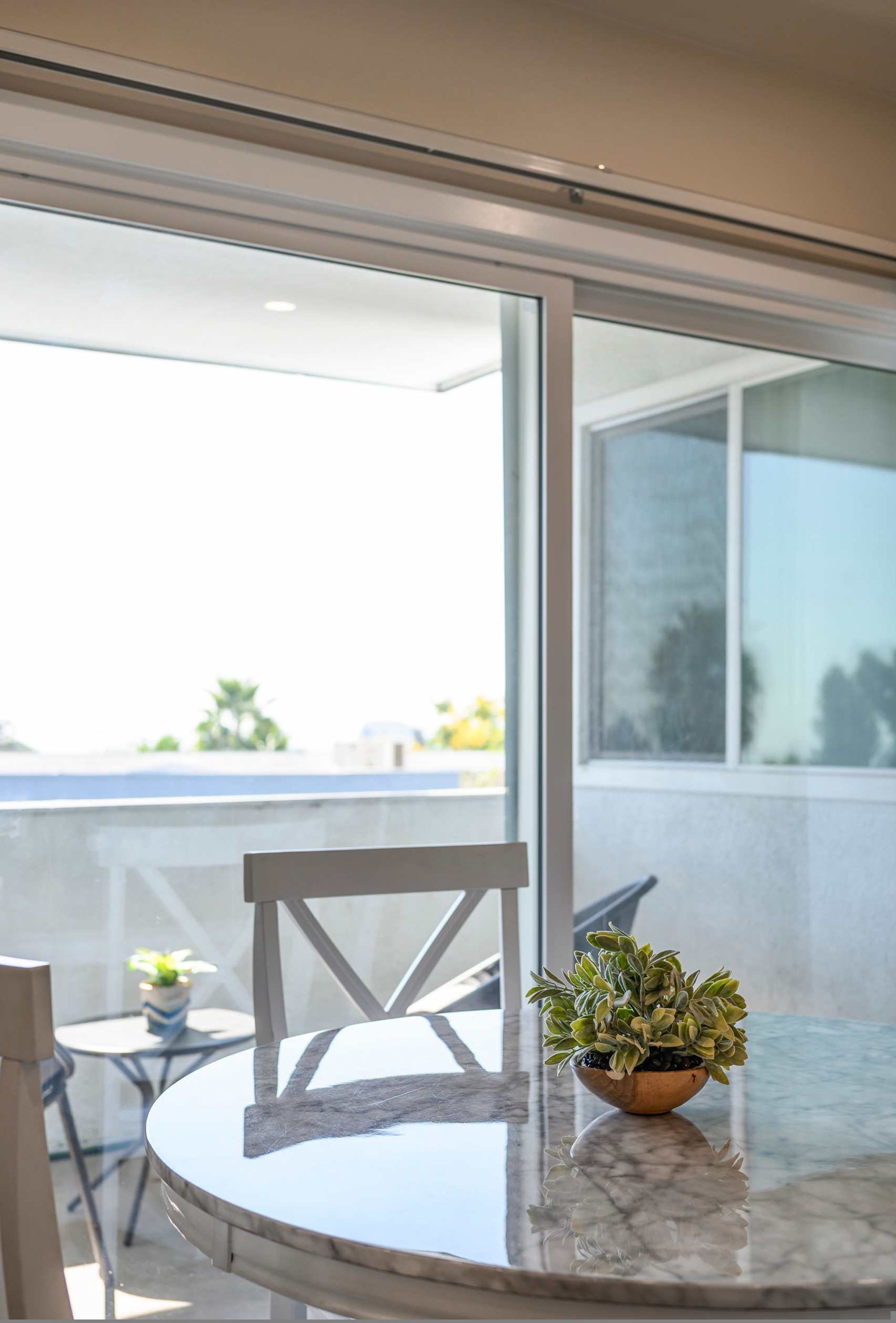 A round marble table with a potted plant, a white chair, and a glass balustrade.