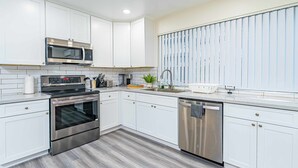 A modern kitchen with white cabinets, stainless steel appliances, and a large window with blinds. - Charming Elegant Retreat in the San Gabriel Valley (Altadena)