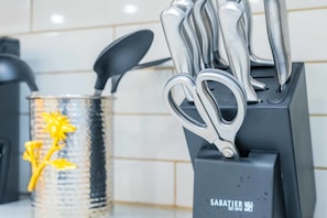 A kitchen utensil holder with a Sabatier logo, a metal pot with a yellow decorative figure, and a black spatula.