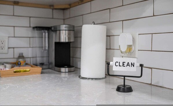 A kitchen with a white tiled backsplash, a coffee machine, a large white candle, and a sign that reads "CLEAN". - Charming Elegant Retreat in the San Gabriel Valley (Altadena)