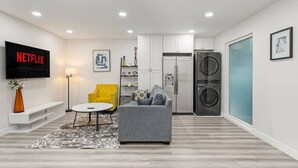 A modern living room with a grey sofa, a yellow armchair, a white coffee table, and a flat-screen TV displaying "NETFLIX". - Charming Elegant Retreat in the San Gabriel Valley (Altadena)