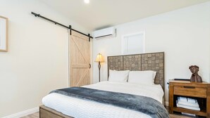 Une chambre à coucher comprenant un lit, une tête de lit en bois, une table de chevet, une lampe et un climatiseur fixé au mur.