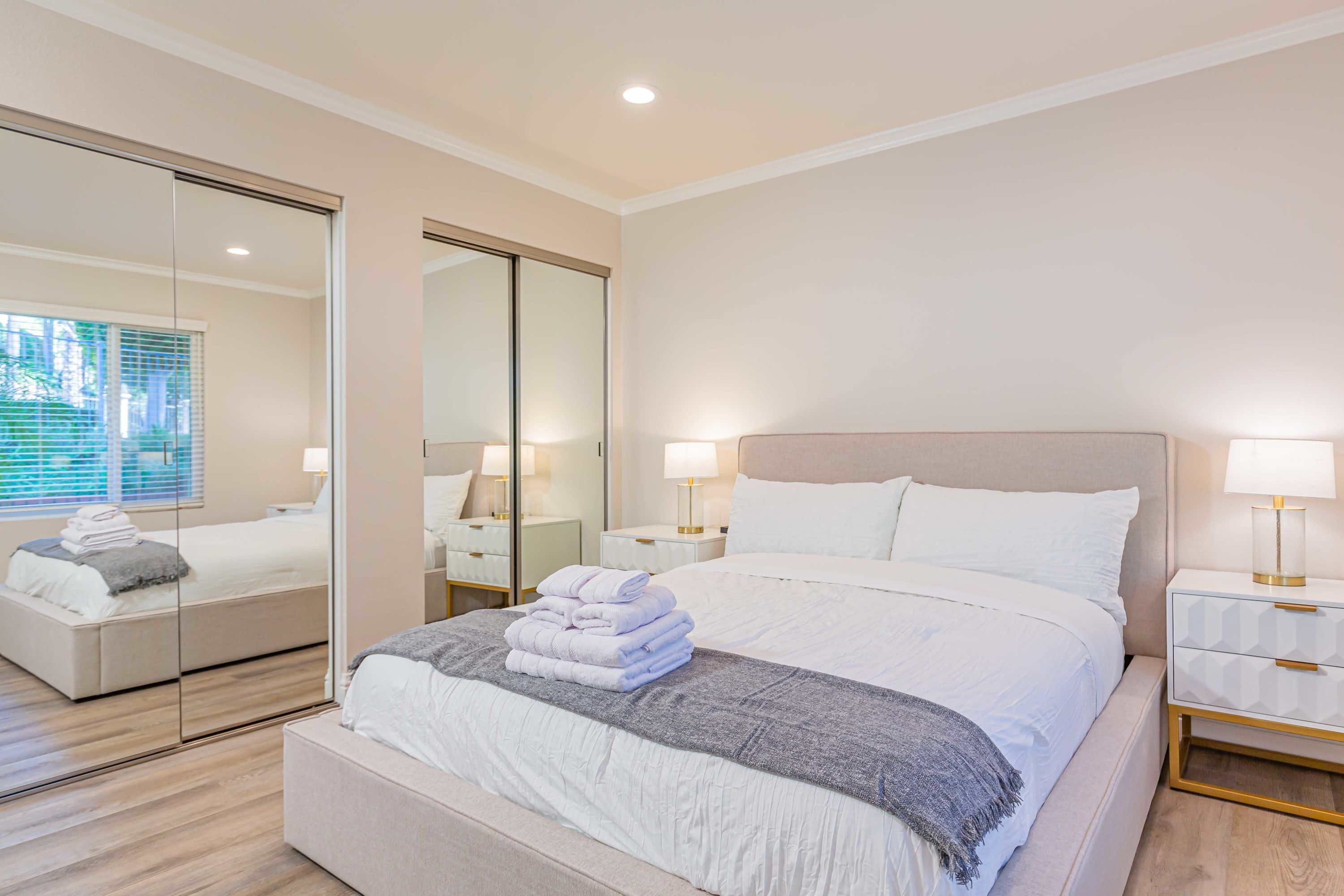 Une chambre d’hôtel moderne avec un grand lit, une table de chevet avec une lampe, un miroir et une armoire.