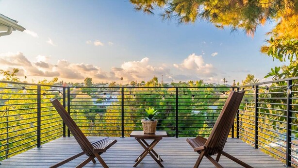 A deck with two wooden chairs and a small table, surrounded by a metal railing with a view of greenery and a clear sky. - Stunning LA Luxury Retreat Ideal for Work or Play (Monterey Park)