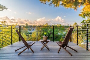 A deck with two wooden chairs and a small table, surrounded by a metal railing with a view of greenery and a clear sky. - Stunning LA Luxury Retreat Ideal for Work or Play (Monterey Park)