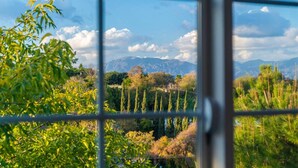 A view through a window with a grid pattern, displaying a landscape with trees, a clear sky, and distant mountains. - Stunning LA Luxury Retreat Ideal for Work or Play (Monterey Park)